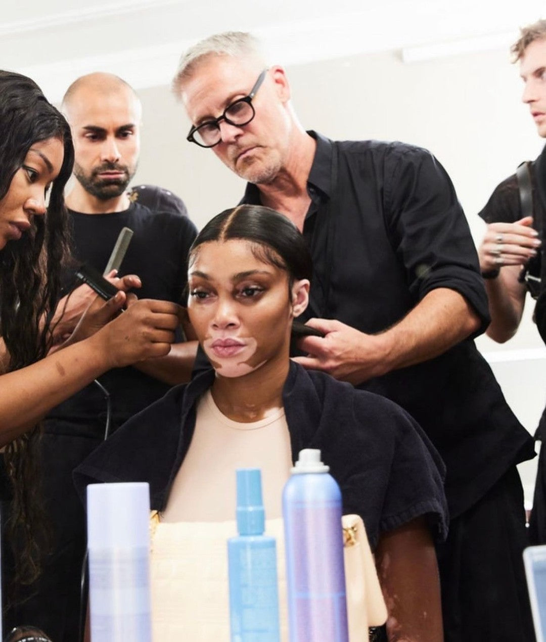 Professionelles Haarstyling-Team stylt ein Model im Backstage-Bereich, verschiedene Haarpflegeprodukte stehen auf dem Tisch davor